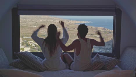 young-fit-millennial-couple-celebrate-amazing-hotel-room-view-in-coastal-European-Greece
