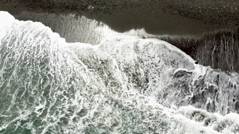 Wellen-Brechen-An-Einem-Dunklen-Sandstrand,-Kontrastierender-Schaum-Und-Texturen,-Luftaufnahme