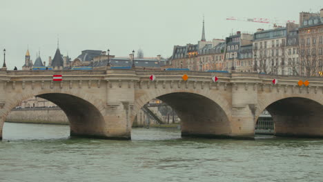 Vista-Diurna-Del-Pont-Neuf-Y-El-Río-Sena-Con-Edificios-Parisinos-En-El-Fondo,-Cielo-Nublado