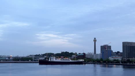 Evening-view-of-a-freight-ship-on-calm-waters-with-city-skyline-and-tower