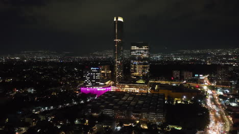 Aerial-view-circling-the-illuminated-Mitikah-tower-complex,-nighttime-in-Mexico