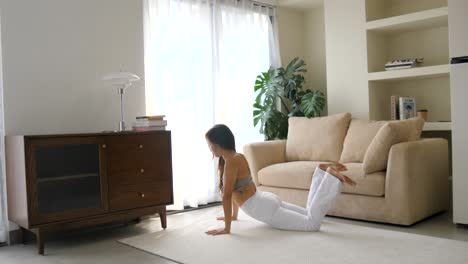 Mujer-Practicando-La-Pose-De-La-Cobra-Real-En-Una-Sala-De-Estar-Minimalista-Y-Soleada,-Con-La-Luz-De-La-Mañana-Filtrándose