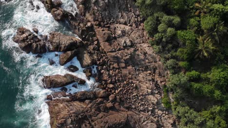 Von-Oben-Nach-Unten-Aufgenommene-Luftaufnahme-Der-Wellen,-Die-Auf-Große-Felsen-Am-Strand-Von-Hiriketiya-In-Sri-Lanka-Krachen