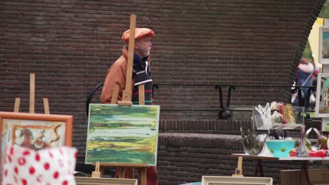Painter-with-orange-beret-and-jacket-among-his-paintings-arranged-on-easels