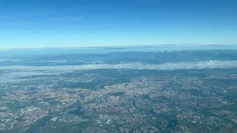 Aerial-view-from-a-jet-cockpit-of-Madrid-city,-Spain,-departing-from-the-airport,-with-some-clouds-in-the-sky-and-snowed-mountains