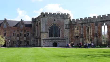 People-visiting-the-Bishop's-Palace-grounds-with-beautiful-green-lawns-in-the-historic-city-of-Wells,-Somerset,-England-UK