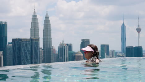 Mujer-Disfrutando-De-Las-Vistas-De-La-Ciudad-Desde-La-Piscina-Infinita-De-La-Azotea-Del-Hotel-En-Kuala-Lumpur,-Malasia