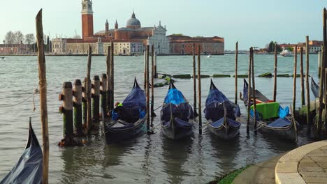 Ein-Venezianischer-Gondoliere-Steigt-In-Seine-Gondel,-Um-Sie-Für-Einen-Arbeitstag-Vorzubereiten,-Während-Im-Hintergrund-Die-Wunderschöne-Kirche-San-Giorgio-Maggiore-Zu-Sehen-Ist