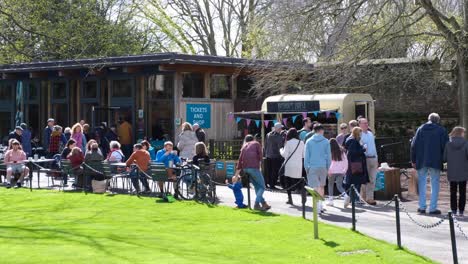 Busy-crowds-of-people-visiting,-walking-and-enjoying-food-and-drinks-inside-the-historic-Bishop's-Palace-grounds-in-the-city-of-Wells,-Somerset,-England