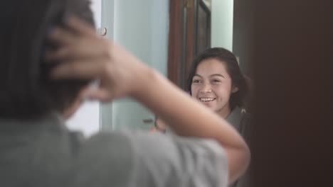 Joven-Latina-En-El-Baño-Peinándose-Y-Sonriendo-Mirándose-En-El-Espejo