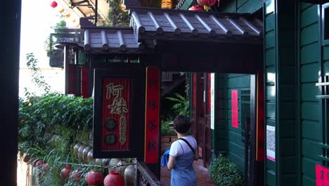 Tourist-taking-photo-with-A-Mei-teahouse-perched-at-the-mountainside-at-Jiufen-Old-Street,-lanterns-hanging-around-the-historic-building-exteriors,-popular-tourist-attraction-in-Taiwan