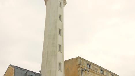 Tall-white-lighthouse-with-green-light-top-in-La-Rochelle-on-a-cloudy-day,-close-up
