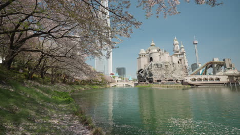 Vista-Frente-Al-Lago-Seokchon-Del-Parque-De-Atracciones-Lotte-World-Y-La-Torre-Lotte-Durante-La-Temporada-De-Floración-De-Sakura-En-Primavera-En-Seúl,-Corea-Del-Sur