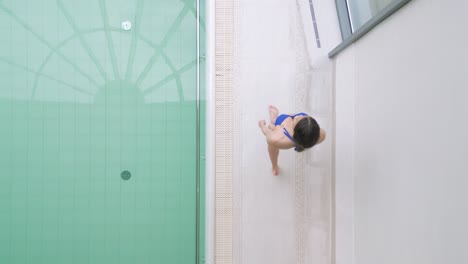 Vista-Aérea-De-Arriba-Hacia-Abajo-De-Una-Mujer-En-Forma-En-Bikini-Caminando-Junto-A-La-Piscina-Cubierta