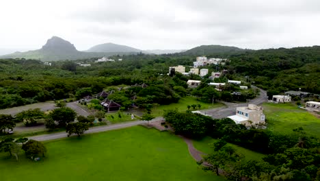 Lush-green-landscape-with-scattered-buildings-under-overcast-skies,-aerial-view