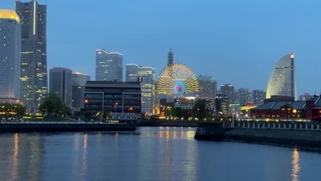 Stadtbild-In-Der-Dämmerung-Mit-Beleuchtetem-Riesenrad-Am-Fluss,-Urbane-Skyline