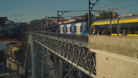 Ponte-Dom-Luis-bridge-in-Porto,-Portugal-shot-at-sunset-while-people-walk-across-and-a-street-car-passes-by