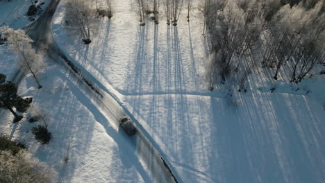 Car-driving-slow-on-icy-slippery-road,-winter-countryside-aerial-from-above