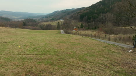 Quaint-green-grassy-hillside-overlooks-rural-country-road-below-forested-mountain