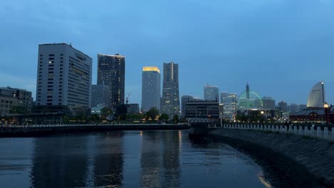 Twilight-cityscape-with-river-reflections,-modern-buildings-glowing-against-dusk-sky,-urban-tranquility