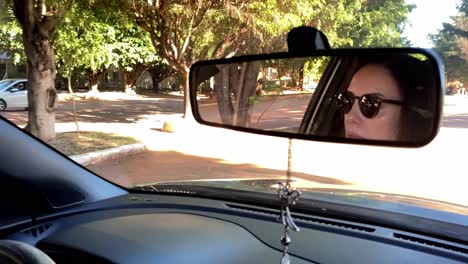 Female-Driver-with-Sunglasses-Reflected-in-Rearview-Mirror,-Slow-Motion