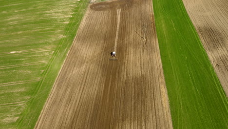 Bird's-eye-view-aerial-follows-tractor-driving-up-center-of-farm-field-harvest