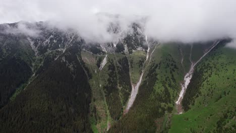 Misty-mountain-peaks-with-snow,-lush-green-valleys-below,-aerial-view
