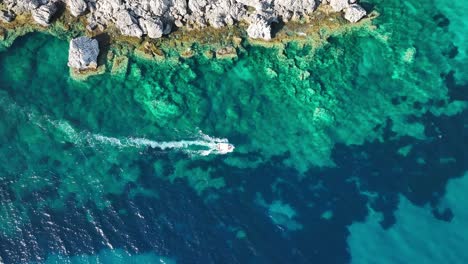 Boat-cuts-through-the-clear-turquoise-waters-by-the-rocky-shores-of-Corfu-Island,-aerial-view