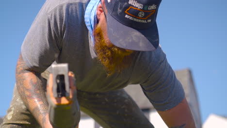 Man-bent-over-using-electric-saw-on-a-hot-day,-low-angle