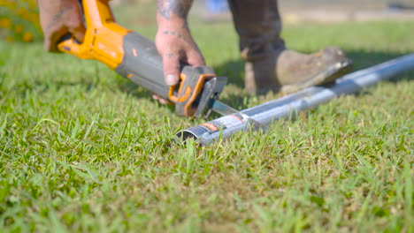 Reciprocating-saw-cuts-metal-pipe-on-the-grass,-close-up