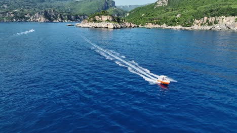 Speedboat-cutting-through-blue-waters-near-Corfu-Island-with-cliffy-coast-in-the-background,-aerial-view