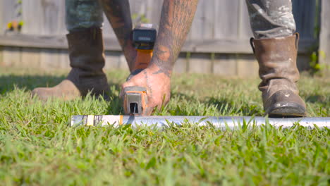 Blue-collar-worker-cutting-pipe-on-the-grass,-low-angle,-orbit