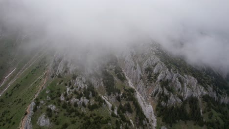 Misty-mountains-with-clouds-rolling-over-rugged-cliffs,-aerial-view