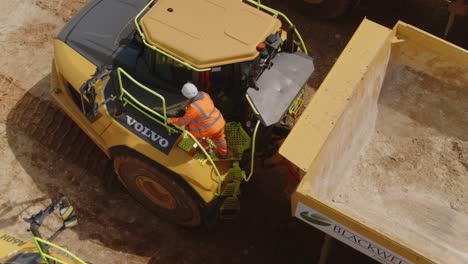 Construction-worker-gets-up-onto-a-dump-truck-to-inspect-its-condition---Top-down-drone-shot