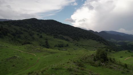 Exuberantes-Colinas-Cerca-De-Un-Pueblo-Bajo-Un-Cielo-Nublado,-Paisaje-Tranquilo-Y-Amplio,-Vista-Aérea