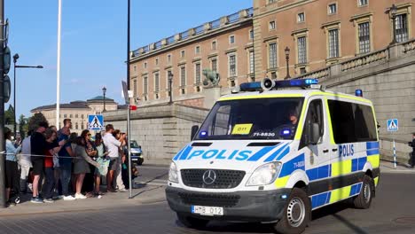 Furgoneta-De-La-Policía-Sueca-En-Movimiento-Con-Turistas-Junto-Al-Palacio-De-Estocolmo-A-La-Luz-Del-Sol,-En-Cámara-Lenta