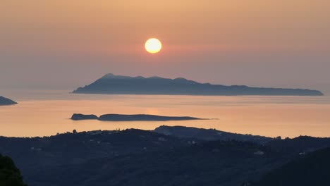 Vista-Del-Atardecer-Sobre-La-Isla-De-Corfú,-Grecia-Con-Un-Sereno-Mar-Iónico-Y-Un-Cielo-Anaranjado.