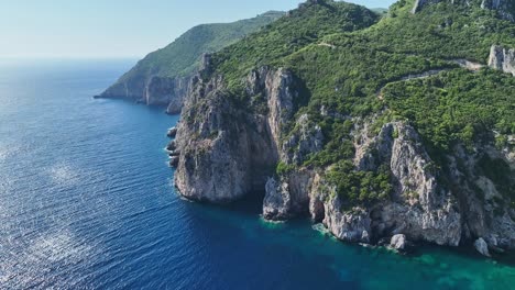 Sunlit-cliffs-on-corfu-island-by-the-ionian-sea,-lush-greenery-on-coastline,-aerial-view