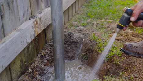 Worker-uses-water-hose-to-mix-concrete-around-metal-post