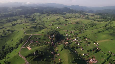 A-quaint-romanian-village-nestled-among-rolling-green-hills,-sunlit,-aerial-view