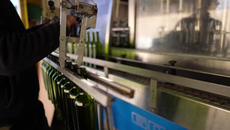 Man-lifting-empty-green-wine-glass-bottles-and-placing-them-in-conveyor-belt,-Slow-motion-pan-right-shot