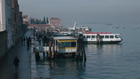 Morning-scene-at-a-Venice-vaporetto-station,-with-locals-and-tourists-navigating-along-the-serene-waterfront