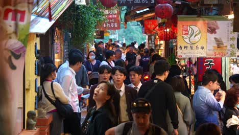 People-strolling-through-narrow-laneway-lined-with-food-stalls,-souvenir-shops-and-gift-stores,-exploring-the-charming-Jiufen-Old-Street-mountain-village-town,-popular-tourist-attraction-of-Taiwan