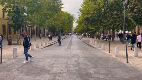 People-walk-and-ride-bikes-on-sidewalk-stroll-along-empty-street-in-Aix-en-Provence