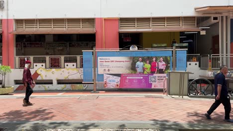 Gente-Caminando-Con-El-Telón-De-Fondo-De-La-Pancarta-De-La-Ministra-Josephine-Teo,-Heng-Chee-How,-Denise-Phua-Y-Wan-Rizal-De-Jalan-Besar-Grc-En-Waterloo-Street,-En-El-Centro-De-Singapur