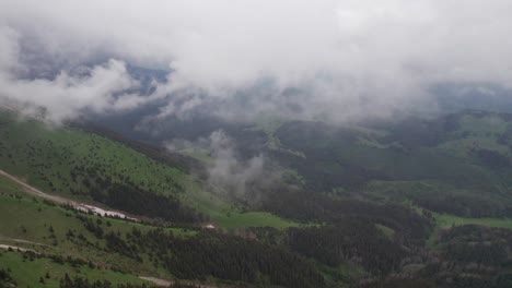 Neblige-Bergkette-Mit-Wolken,-Die-über-Leuchtend-Grünen-Hängen-Schweben,-Luftaufnahme