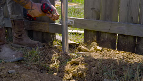 Skilled-worker-with-tattooed-arms-using-electric-drill-to-repair-privacy-fence-outdoors