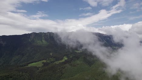 Misty-clouds-rolling-over-lush-green-mountains,-aerial-view