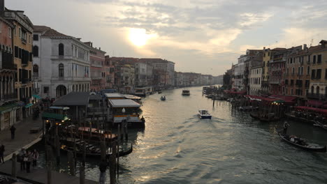 View-of-Grand-Canal-with-boat-sailing,-sun-setting-between-clouds,-Venice