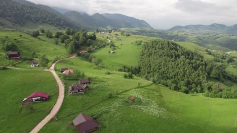 A-serene-mountain-village-with-winding-roads-and-lush-greenery,-shot-in-daylight,-aerial-view